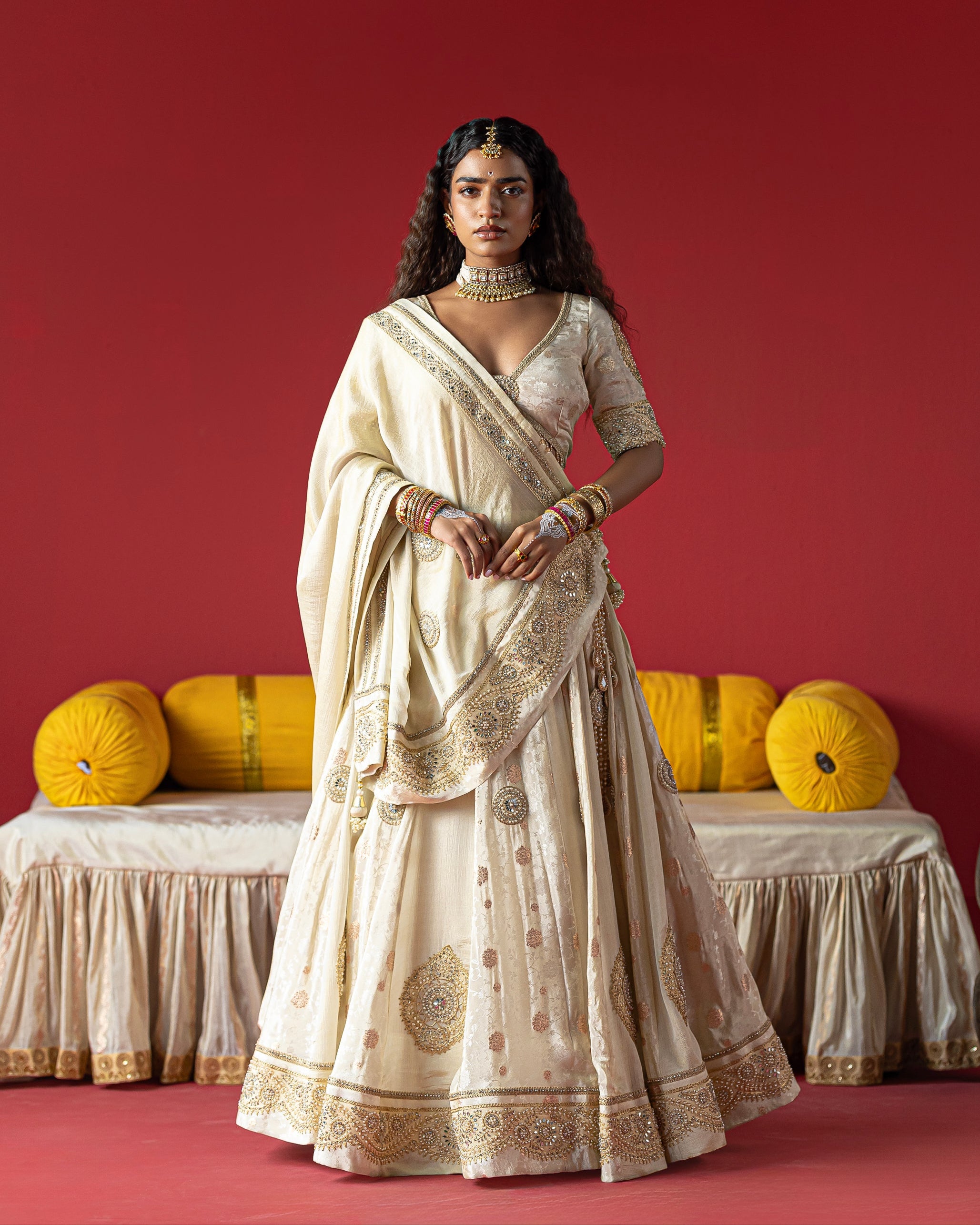 Woman in a traditional cream saree with gold patterns against a red background