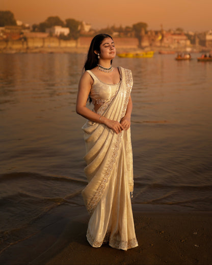 Woman in a traditional saree standing by a river with a cityscape in the background