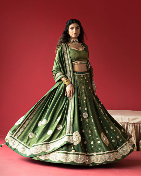 Woman in a green traditional outfit with intricate designs on a red background